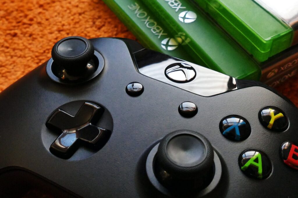 Um controle do Xbox fica no chão ao lado de uma pilha de jogos do Xbox One.